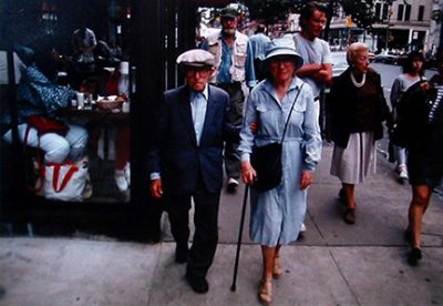 Photo of Richard Nagler's photograph "Homage to Raphael Soyer, NYC, September 1987." Artwork depicts people walking on a busy city street, man and a woman with a cane at center.