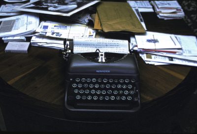Richard Nagler's photograph "Isaac's Typewriter, Miami Beach July 1990." Artwork depicts a Remington typewriter on a table. Papers and letter cover much of the table surface.