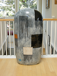 Photo of Jun Kaneko's ceramic sculpture "Untitled, Dango." Image depicts a grey monolith with a rounded top. Background color is grey with squares of color and groupings of black drips.