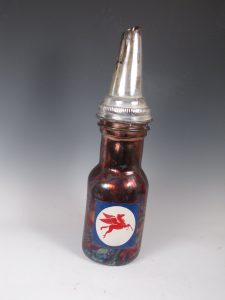 Karen Shapiro "Mobile Oil" raku-fired ceramic of vintage canister. Red, white, and blue label with a pegasus, brown bottle shaped body with a silver pour spout.