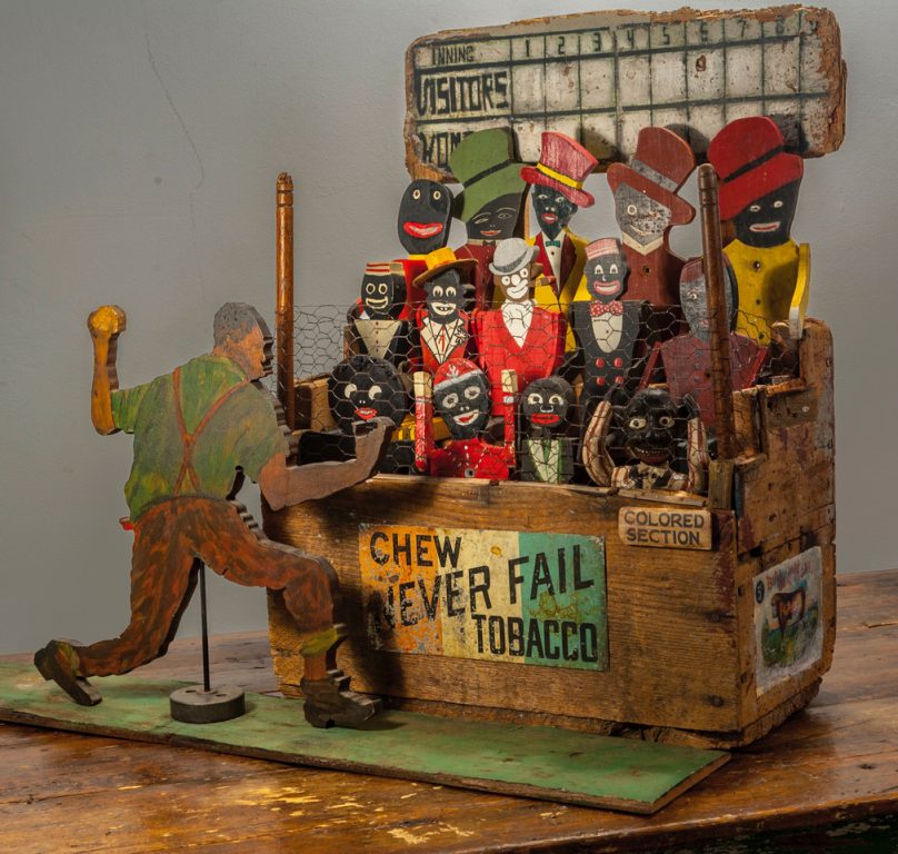 Sculpture constructed from an old wood farrier's box and peopled with racist stereotype “Dancing Dan” toy figures. Handmade & painted carved wood African American pitcher.