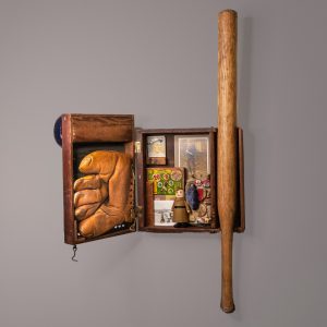 Antique tin baseball game sculpture forms the treasure chest of a boy in a baseball uniform. Old baseball cards, mitt, bat, punch game, vintage Wilson Walkie toy, vintage campaign pin, soldier's cap, WWII medal, vintage photo of soldiers playing baseball. On the side is a vintage photo of a young Black soldier.