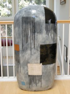 Jun Kaneko's glazed ceramic sculpture of a rounded rectangle, with grey, black, blue, cream, orange, and brown squares painted throughout.