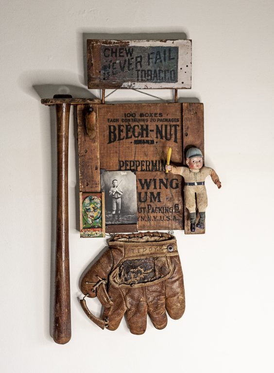 Kat Flyn's sculpture "Teddy" made of old Beechnut gum backboard with advertisement for tobacco on top, vintage bat, vintage glove with Teddy hand printed on strap, old photo of boy in baseball uniform, old doll ballpark souvenir, vintage toy handheld pinball game, old rabbits foot.