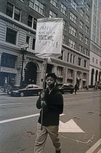 Photo of Richard Nagler's photograph "Make America Think Again." Artwork depicts a person holding a protest sign in downtown Oakland, CA in black and white.