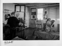 Black and white photograph of Ferlinghetti in his art studio painting a seated nude model.