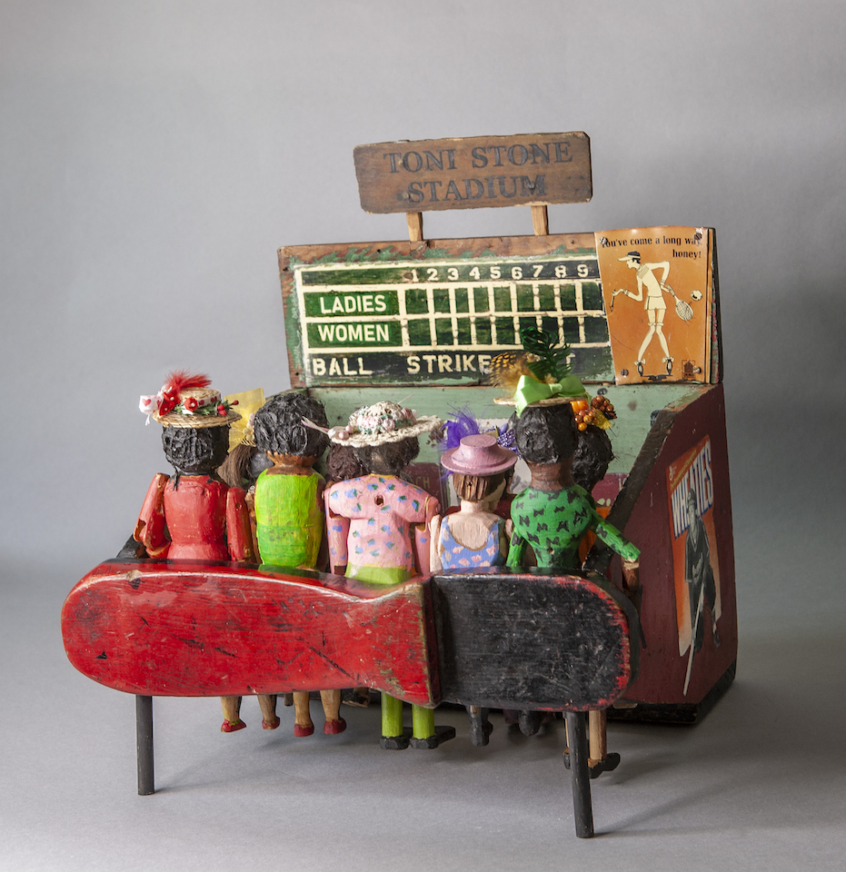 Assembled sculpture of a crowd of women watching a baseball game with a scoreboard and signage that says Toni Stone Stadium