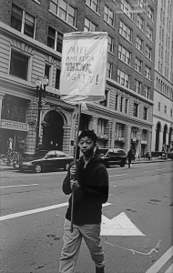 Black and White photograph of a protester holding a sign with the phrase Make America Think Again!