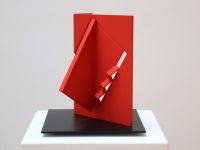 Steel sculpture of a red rectangular shape with a protruding corner of a triangle and cut out zig zag in the center