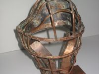 Photo of Ken Kalman's sculpture "Catcher's Mask." Artwork depicts a baseball catcher's mask made of copper.