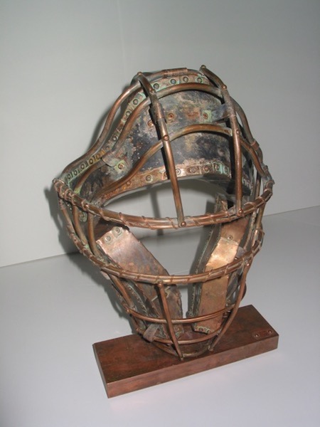Photo of Ken Kalman's sculpture "Catcher's Mask." Artwork depicts a baseball catcher's mask made of copper.