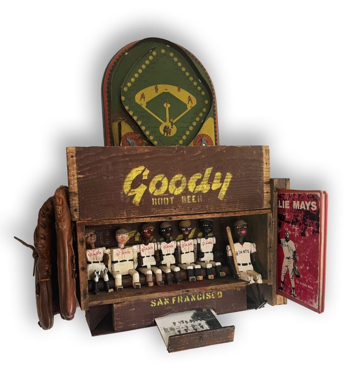 Vintage Goody soft drink box fashioned into a dugout with hand carved & painted wood kid baseball players and an adult BB player inside. Surrounding the dugout are vintage baseball artifacts including a tin baseball game, vintage Willie Mays picture book from a school library, vintage Willie Mays baseball glove and a pullout drawer at the bottom containing an original photo of Black & white kids in baseball uniforms and a vintage well loved Dave Pope baseball card.